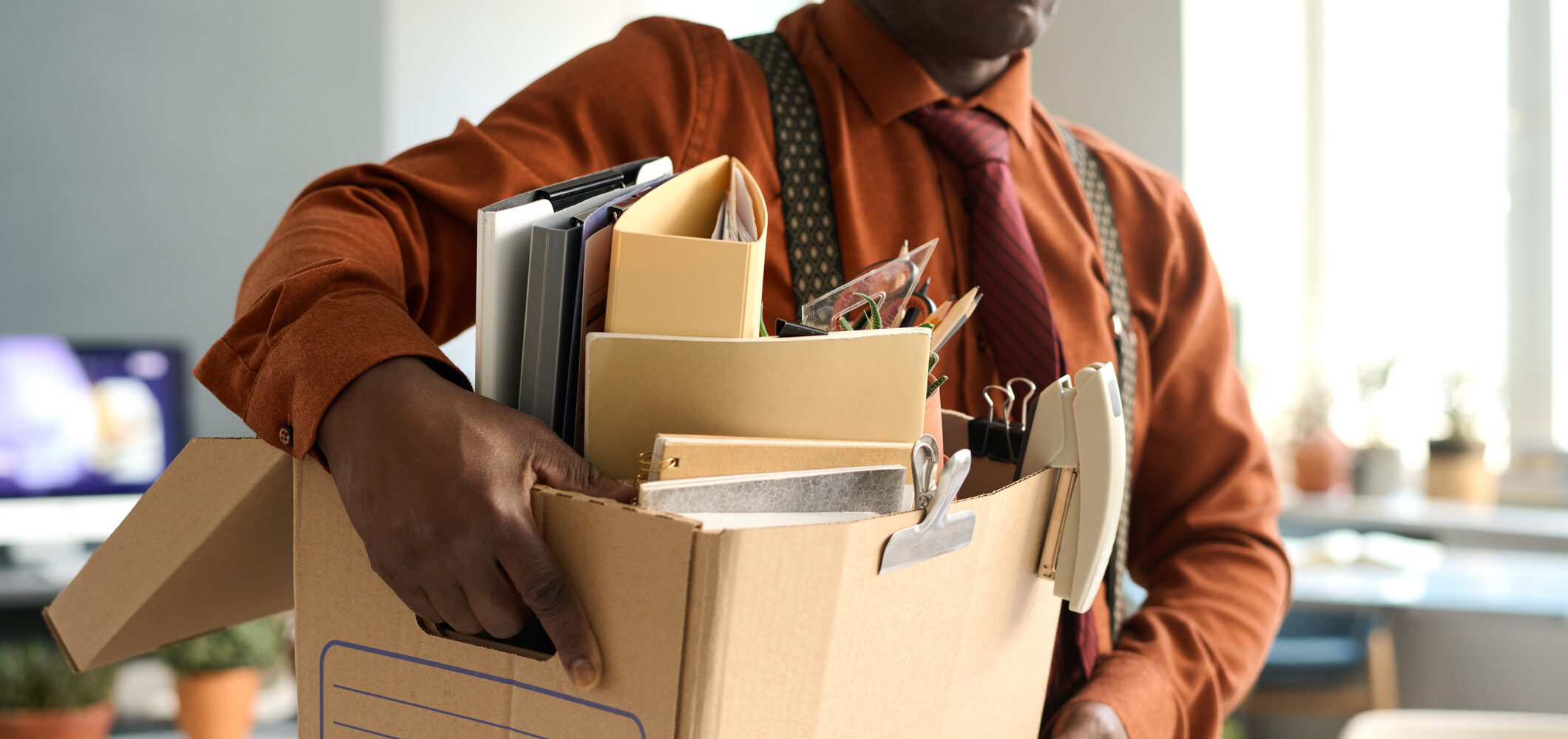Senior man holding box with personal items leaving office workplace after layoff