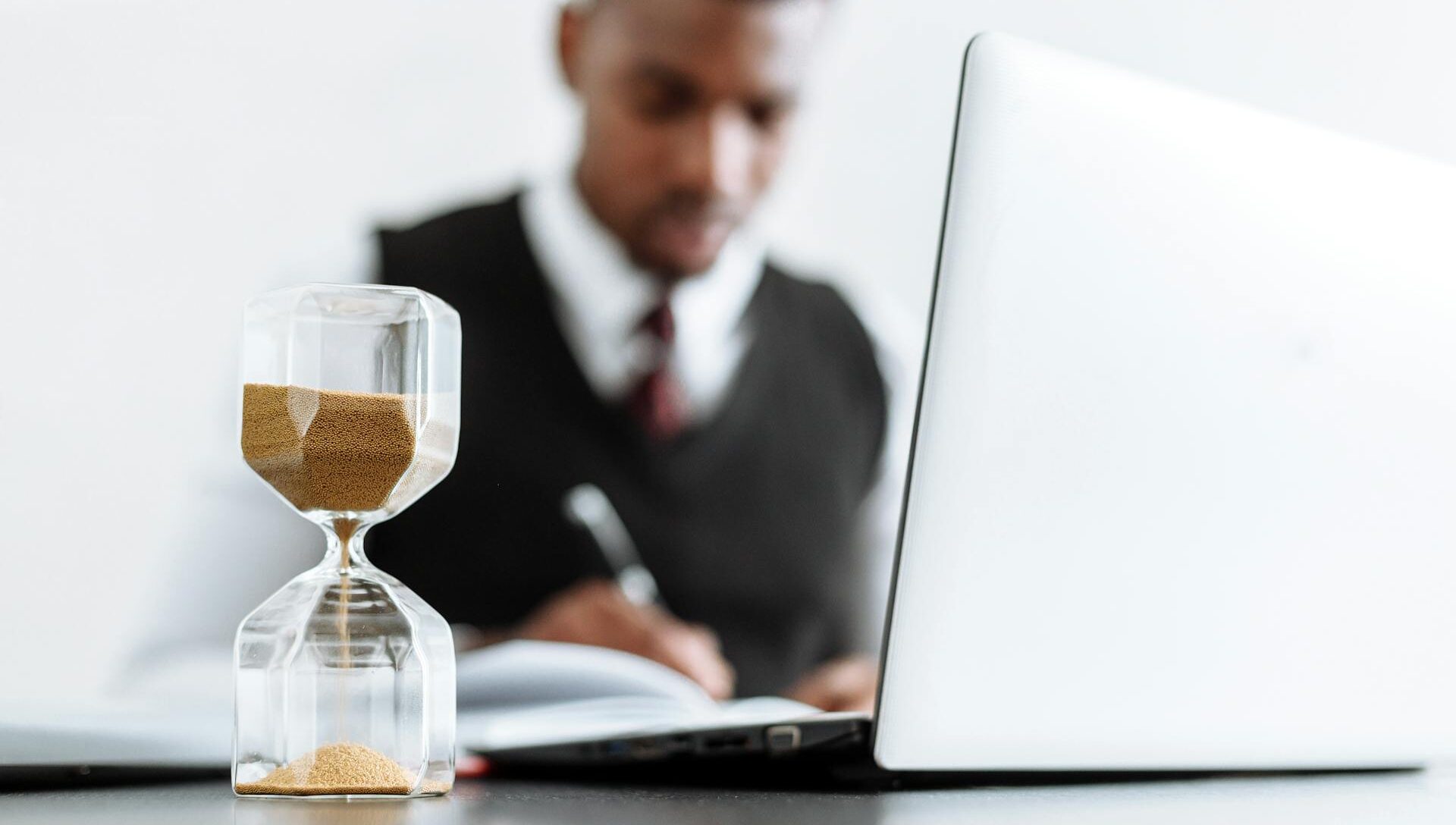 man on laptop with an hourglass on the desk